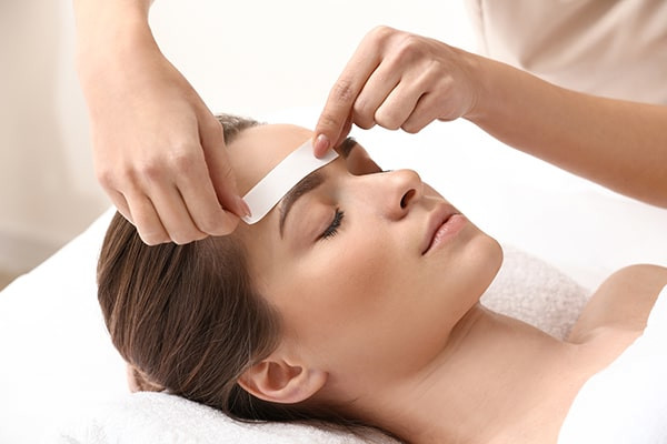 Young woman undergoing eyebrow correction procedure in beauty salon